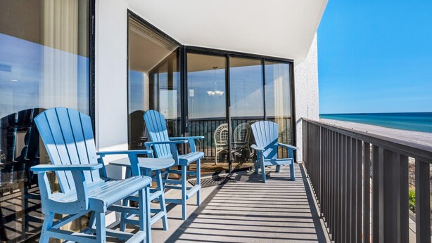 Un balcone con poltrone Adirondack blu, una porta vetrata che dà su una stanza e vista sull'oceano.