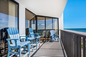 A balcony with blue Adirondack chairs, a glass door leading to a room, and a view of the ocean. - Aquavista 404w (Panama City Beach)