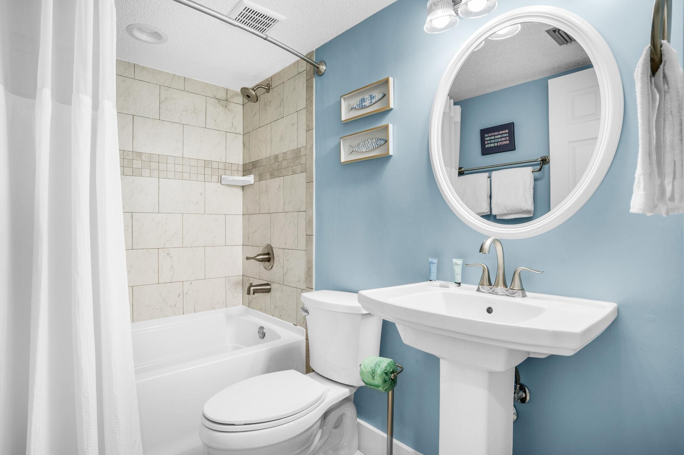 A bathroom with a bathtub, toilet, and sink. There are two framed fish decorations on the wall.