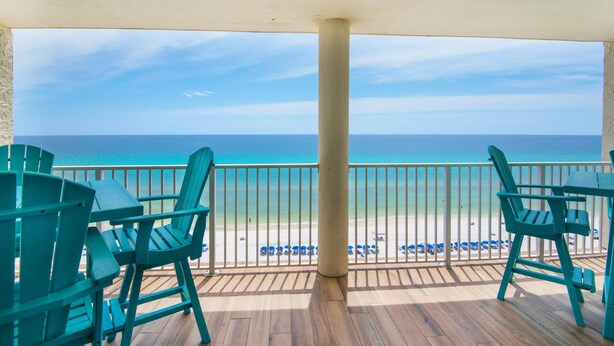Una terraza de madera con sillas turquesas y vista a la playa.