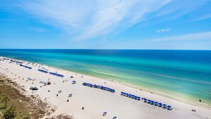 Una playa con hileras de sombrillas azules y sillas de playa, una orilla arenosa y el océano.