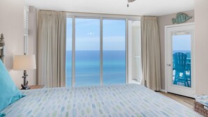 Un dormitorio con una cama grande, un ventilador de techo y vista al océano a través de una puerta corrediza de vidrio.