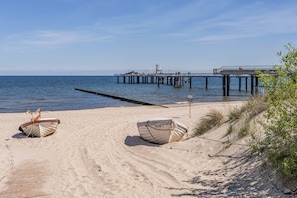Ein Strand mit zwei Booten, einem Steg und blauem Himmel.
