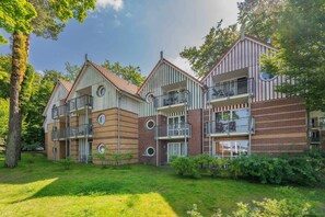 Un immeuble résidentiel à plusieurs étages, doté de balcons, d’une façade en briques et entouré d’une zone verdoyante.