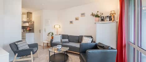 Ein modernes Wohnzimmer mit einer Couch, Sesseln, einem Couchtisch und einer Küche im Hintergrund.