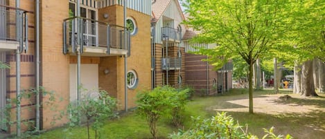 Ein Mehrfamilienhaus mit mehreren Balkonen, einer Ziegel-Fassade und einem kleinen Garten mit Bäumen und Sträuchern.