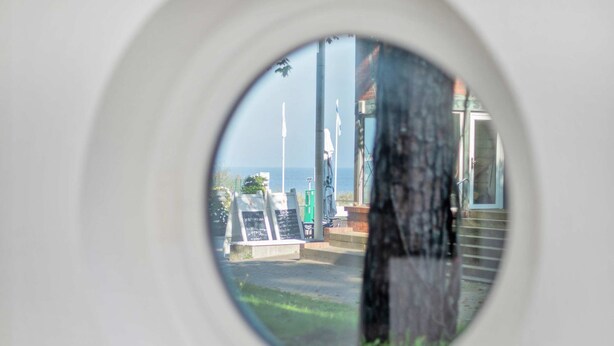 Rundblick aus einem Fenster auf ein Gebäude mit einer Schautafel und einer Fahnenstange.