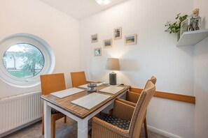 Un coin repas avec une fenêtre ronde, une table entourée de chaises, une lampe et des tableaux encadrés accrochés au mur.