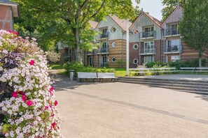 A multi-story residential building with balconies, a paved courtyard, and flower beds.