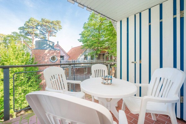 A balcony with white plastic chairs and a table, a blue and white striped wall, and a brick building in the background.
