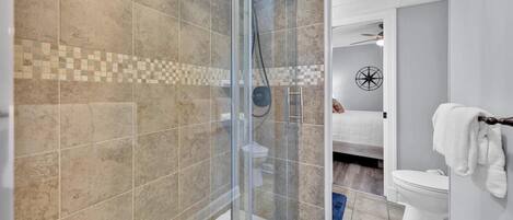 Een moderne badkamer met een douchecabine van glas, een wit toilet en een blauwe badmat.