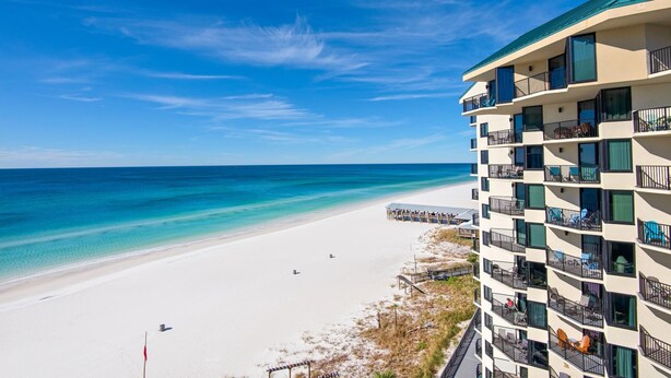 A beachfront hotel with balconies overlooking the ocean, a sandy beach, and a clear sky. - Sunbird 1010e (Panama City Beach)