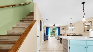 Une cuisine moderne avec des meubles de couleur bleu clair, un escalier en bois et un coin repas agrémenté de rideaux bleus.