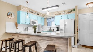 Une cuisine avec des meubles de couleur bleu clair, un plan de travail blanc et des tabourets en bois.