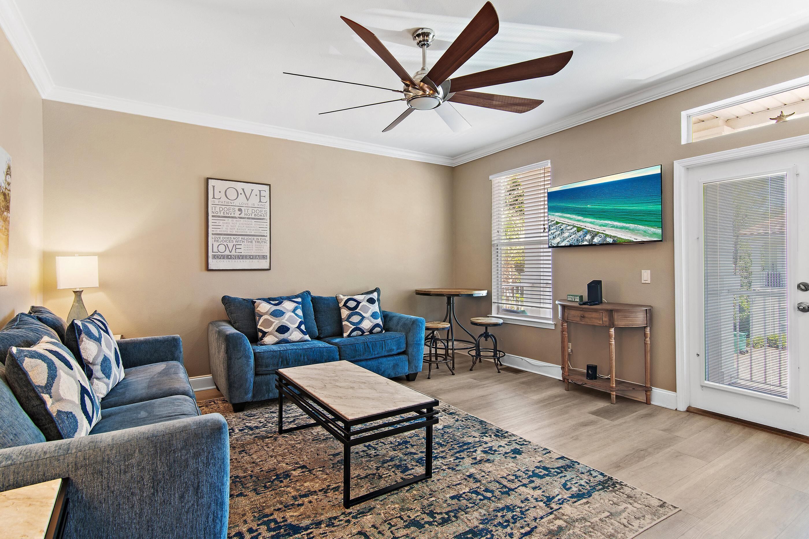 A living room with a ceiling fan, a blue sofa set, a coffee table, a rug, a TV, and a window with blinds.