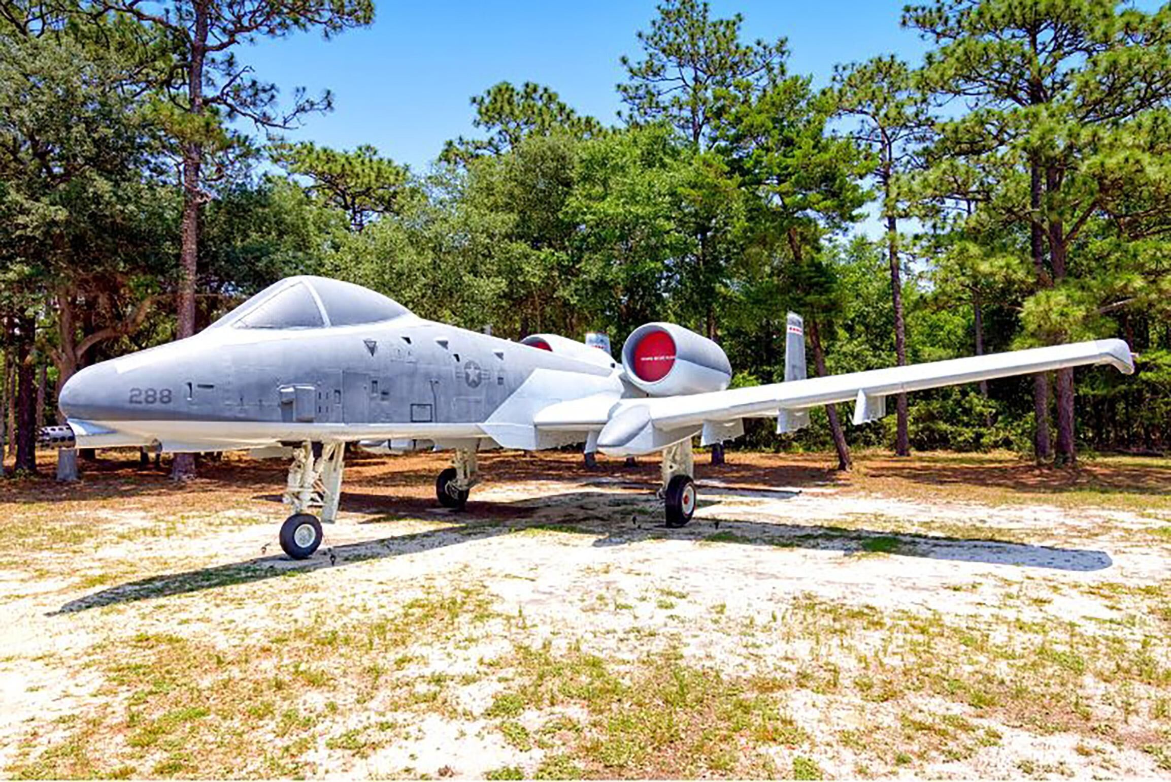A military aircraft on display outdoors with trees in the background.