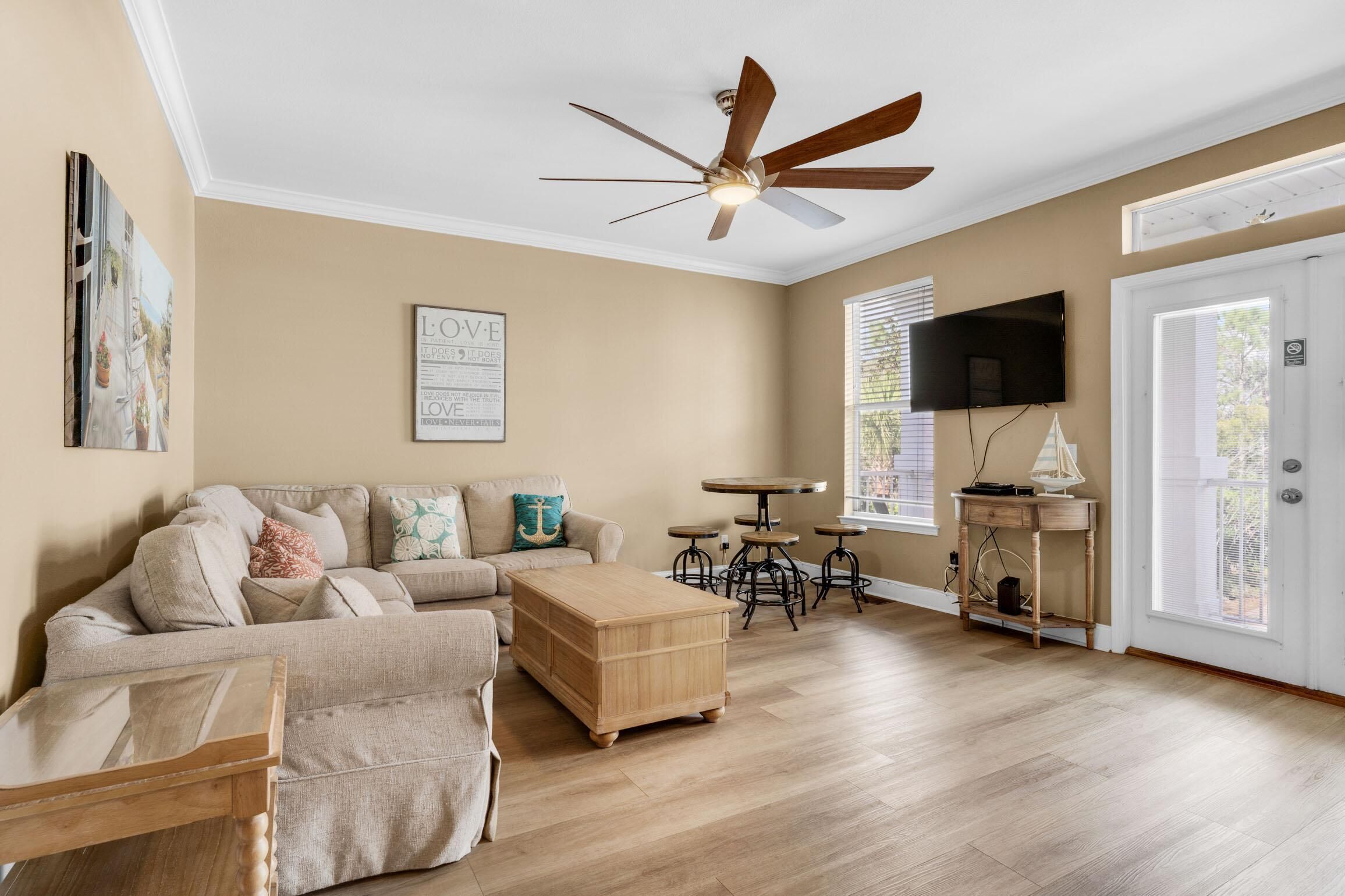 A living room with a sectional sofa, a wooden coffee table, a ceiling fan, a TV, and a window with blinds.