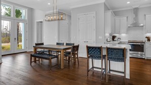 Una cocina moderna con armarios blancos, electrodomésticos de acero inoxidable y un comedor con mobiliario de madera y sillas tejidas.