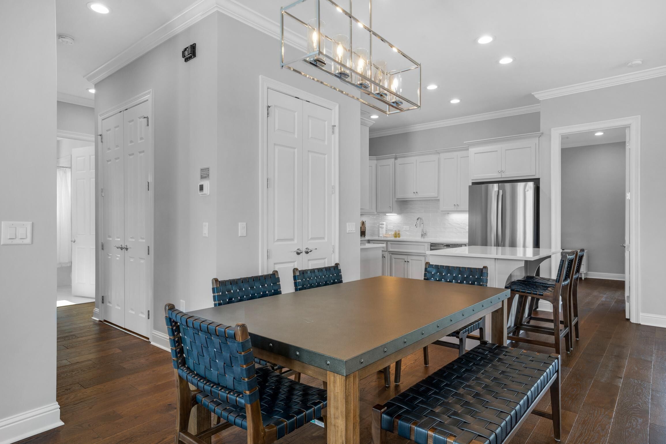 A spacious kitchen with white cabinets, a stainless steel refrigerator, and a dining area with a wooden table and blue upholstered chairs.