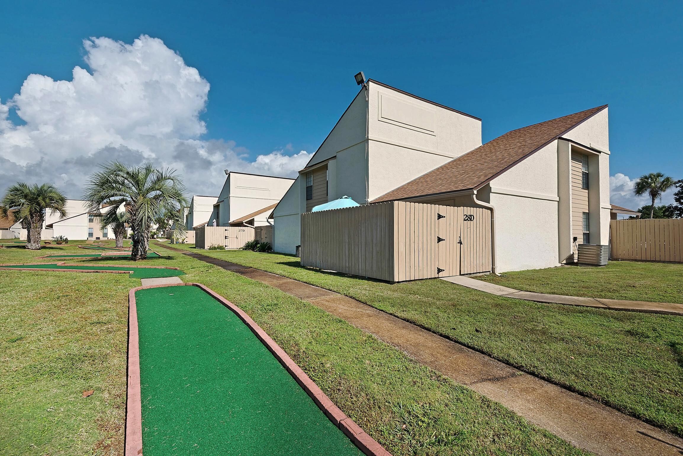 A residential area with modern houses, a green artificial turf path, and a clear blue sky.