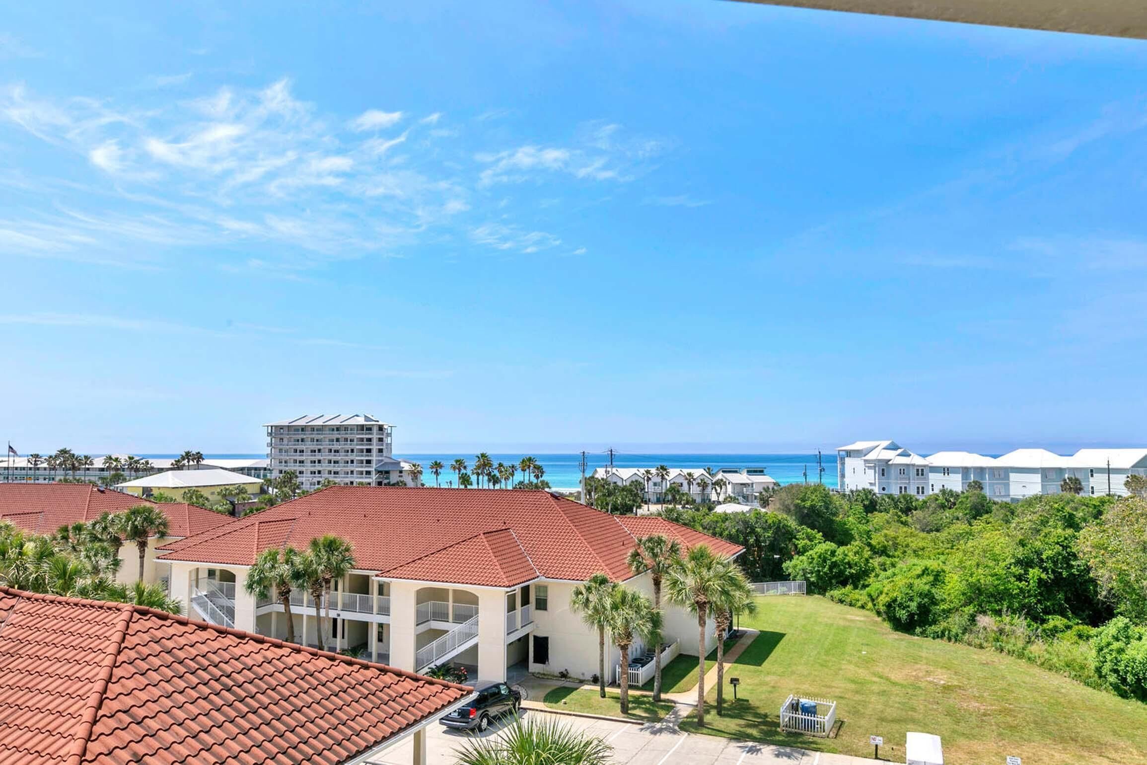 A coastal hotel with red-tiled roofs, a parking area, and a view of the ocean.