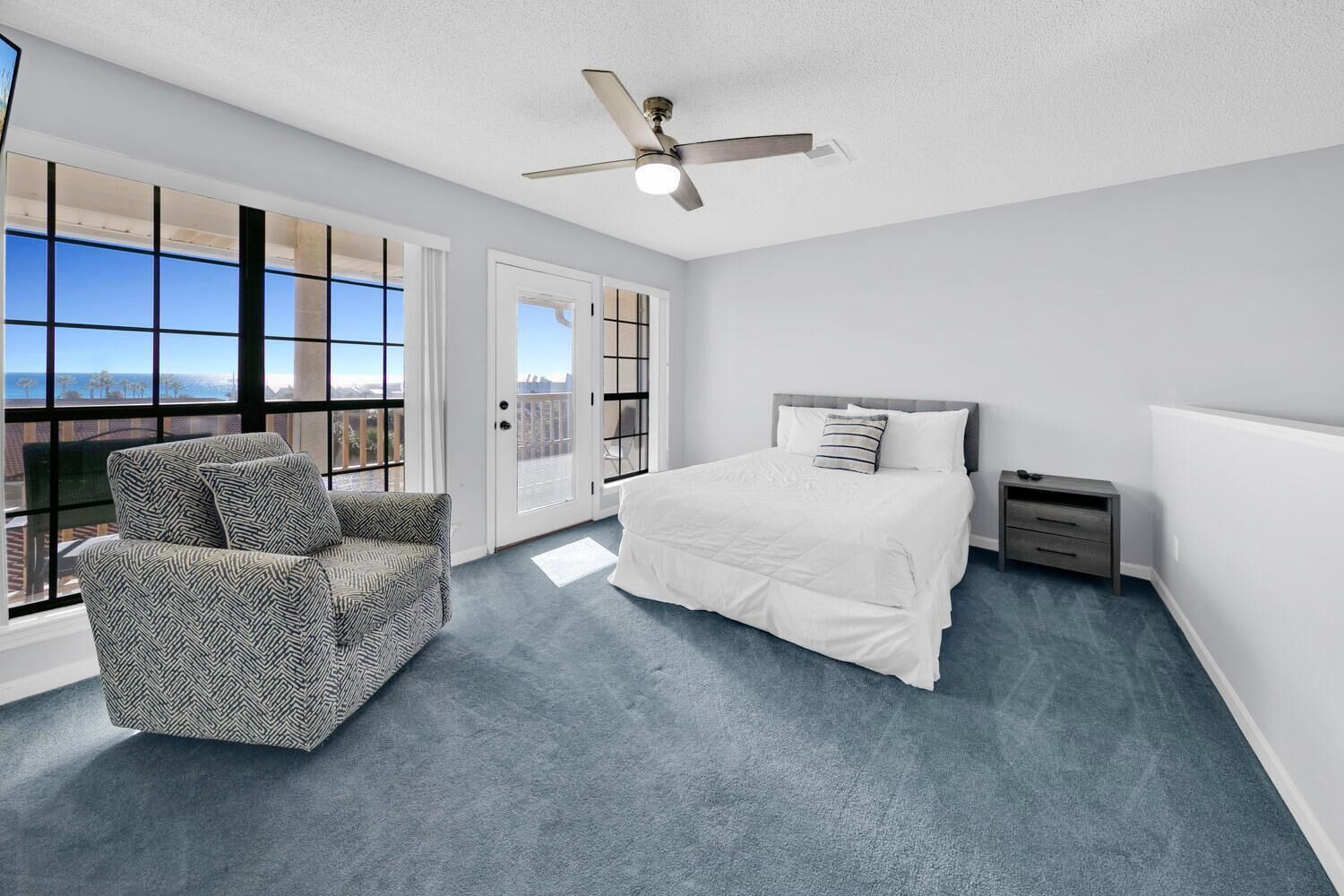 A bedroom with a bed, a chair, a nightstand, and a ceiling fan.