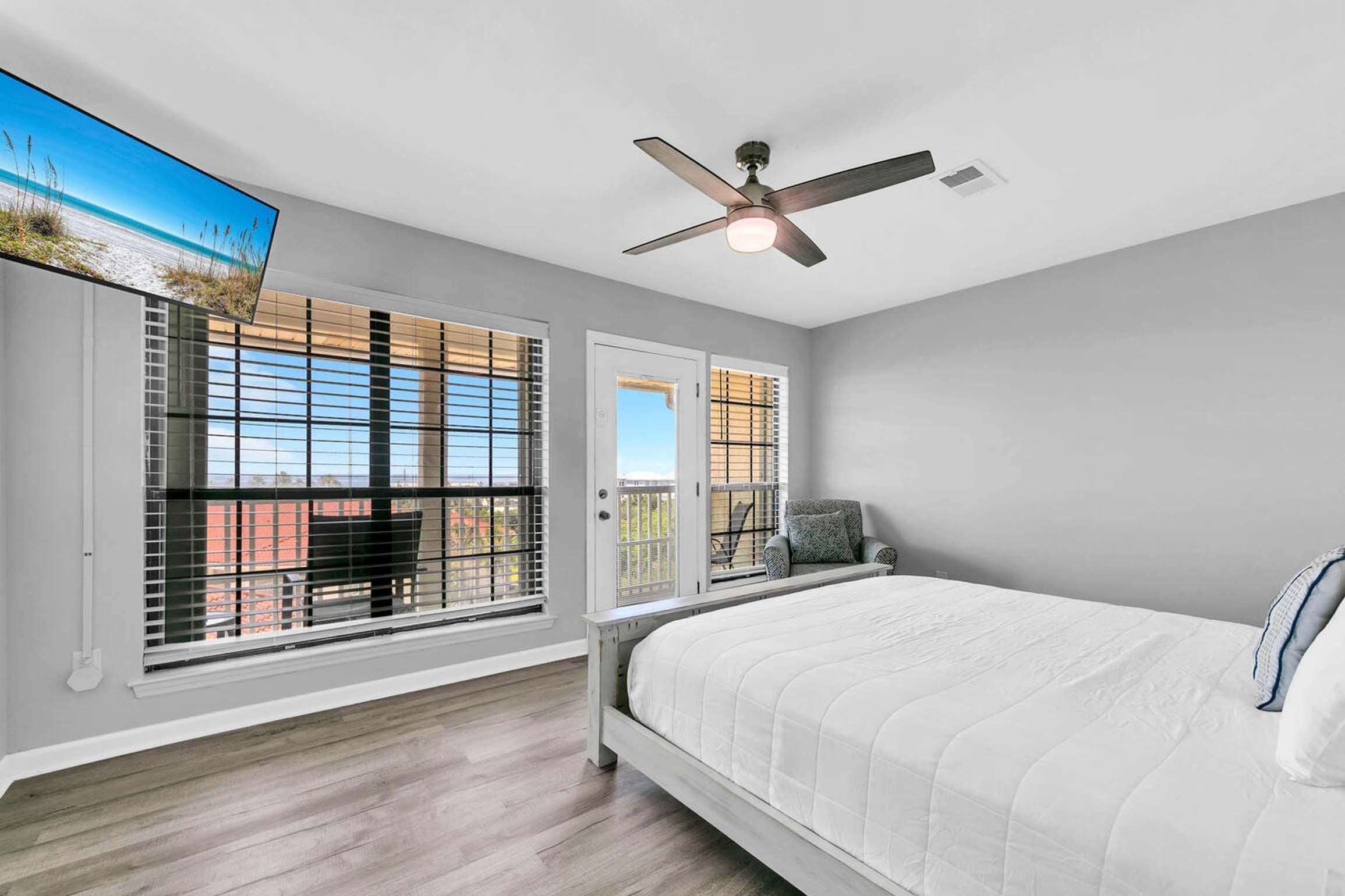 A bedroom with a bed, a ceiling fan, and large windows with blinds.