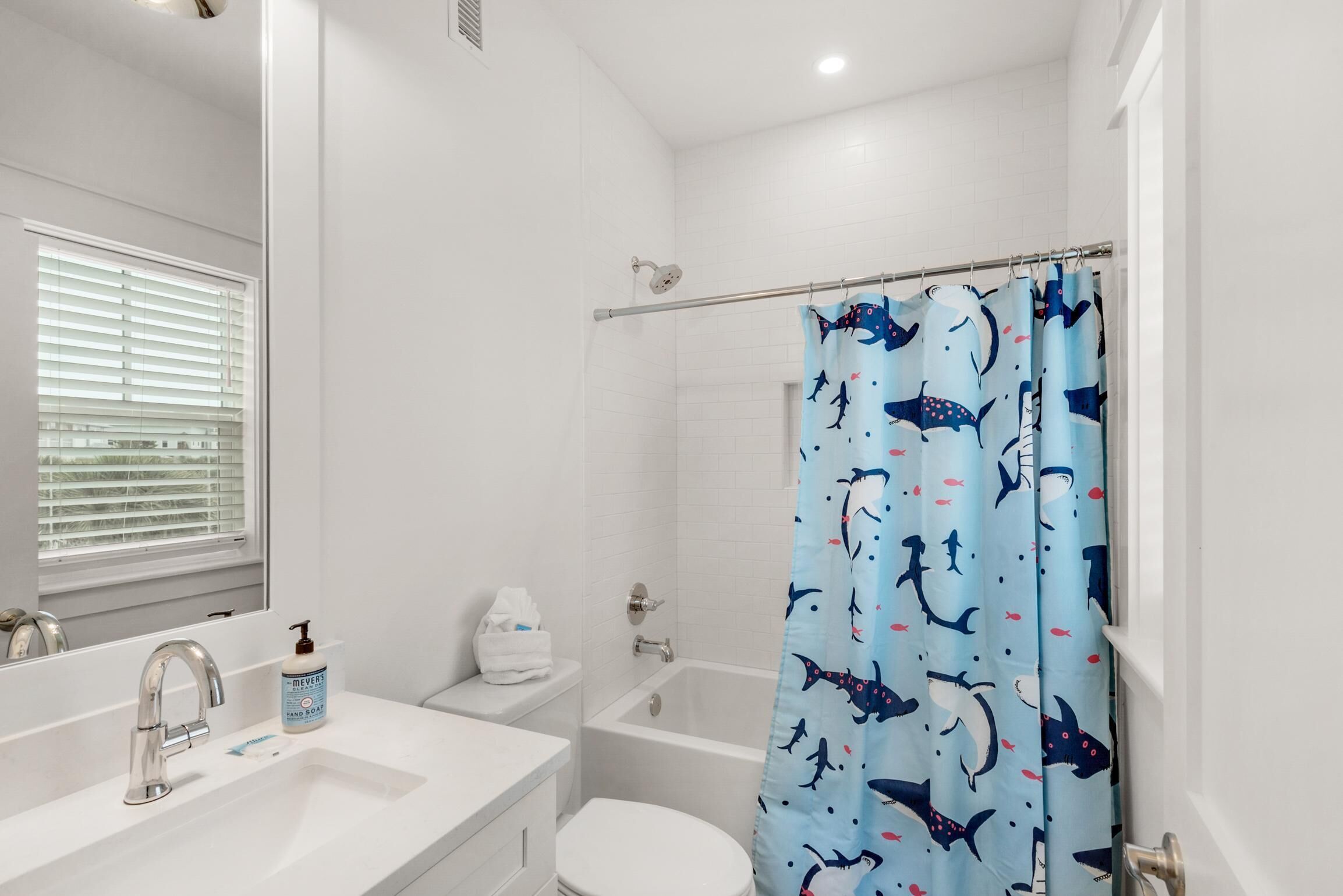 Une salle de bain avec un lavabo blanc, un miroir, des toilettes, une baignoire et un rideau de douche orné d’un motif de requin.