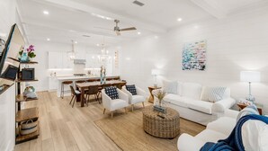 A modern living room with a white sofa, a dining area with a wooden table, and a kitchen in the background.