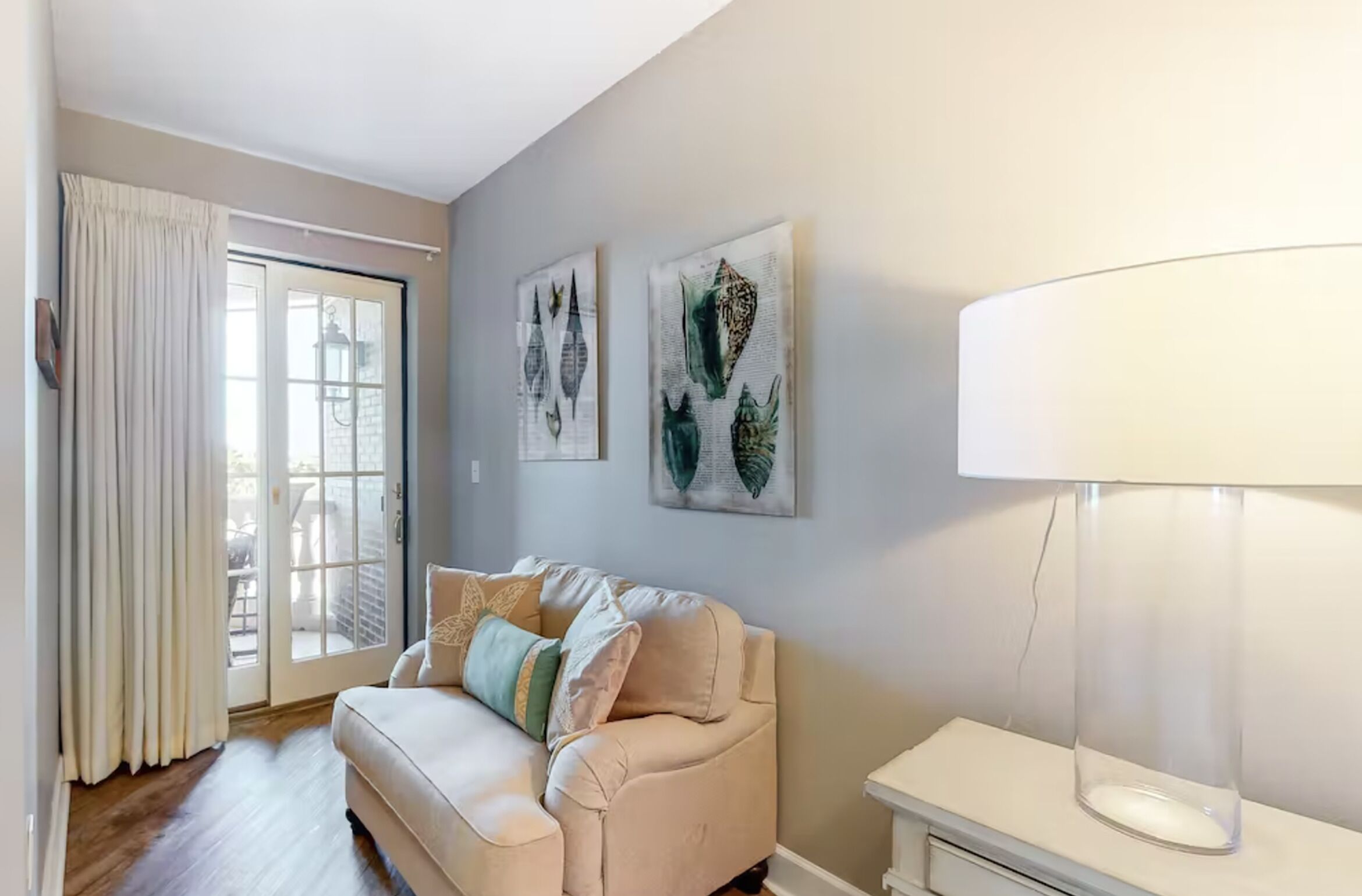 A living room with a beige sofa, a glass coffee table, and artwork on the wall.