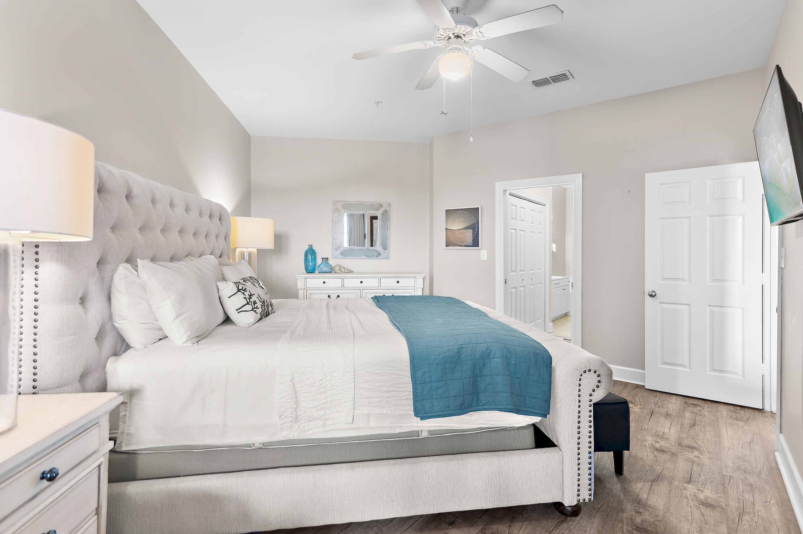 Une chambre à coucher avec un lit, des tables de chevet, un ventilateur de plafond, un miroir et une porte.