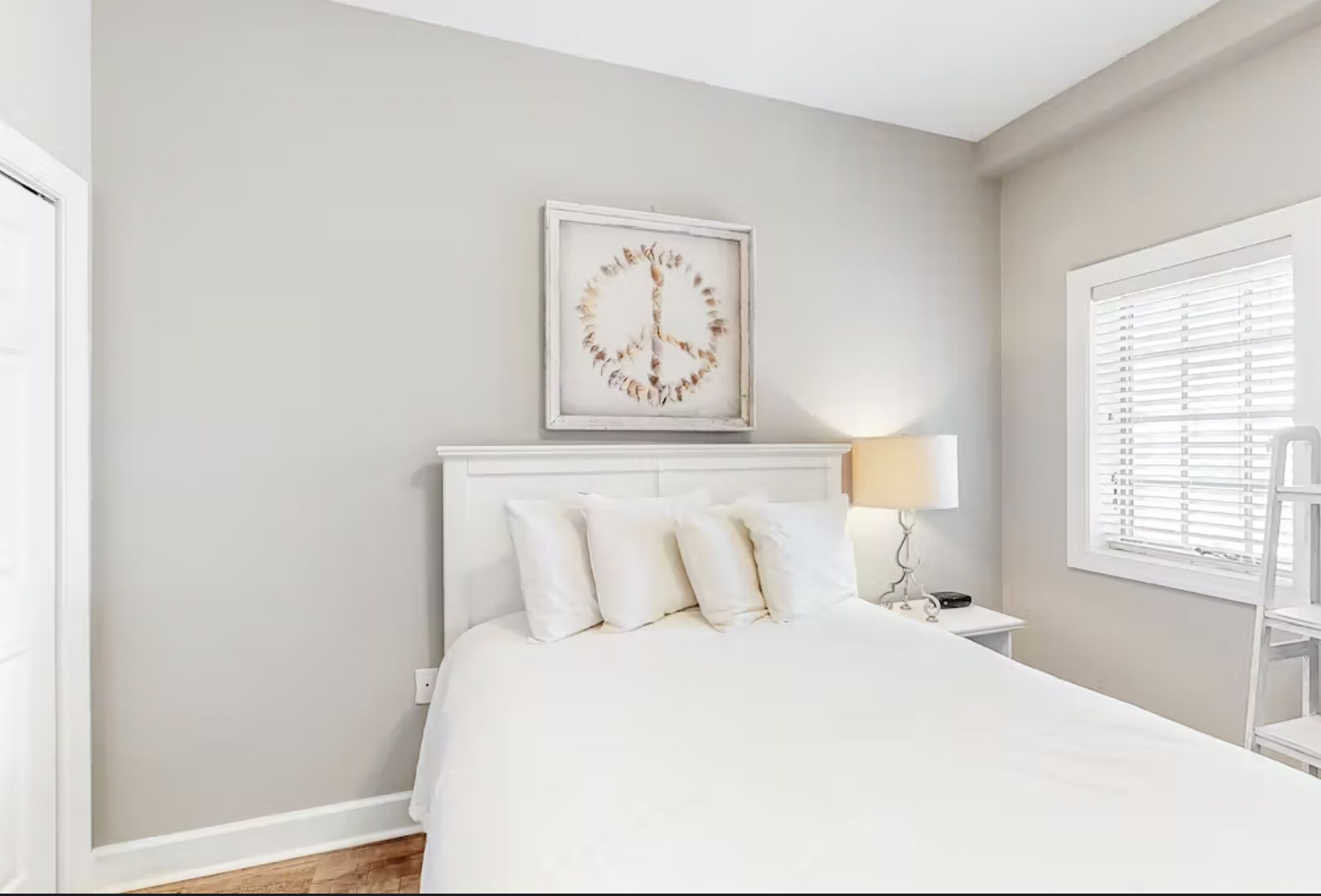 A bedroom with a bed, white headboard, bedside table, lamp, and a framed artwork on the wall.