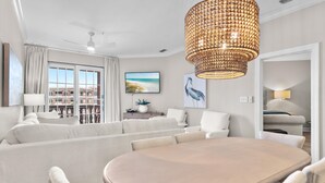 A modern living room with a round table, white sofas, a large window with a view, and a decorative chandelier.