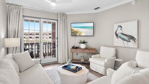 A modern living room with a sofa, armchairs, a coffee table, a TV, and a balcony with a view.