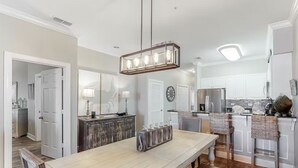 A spacious kitchen with a long wooden table, hanging light fixture, and white cabinetry.