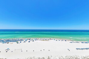 A beach with rows of beach umbrellas and sun loungers, a volleyball net, and a clear view of the ocean. - Long Beach Resort 1-1203 (Panama City Beach)