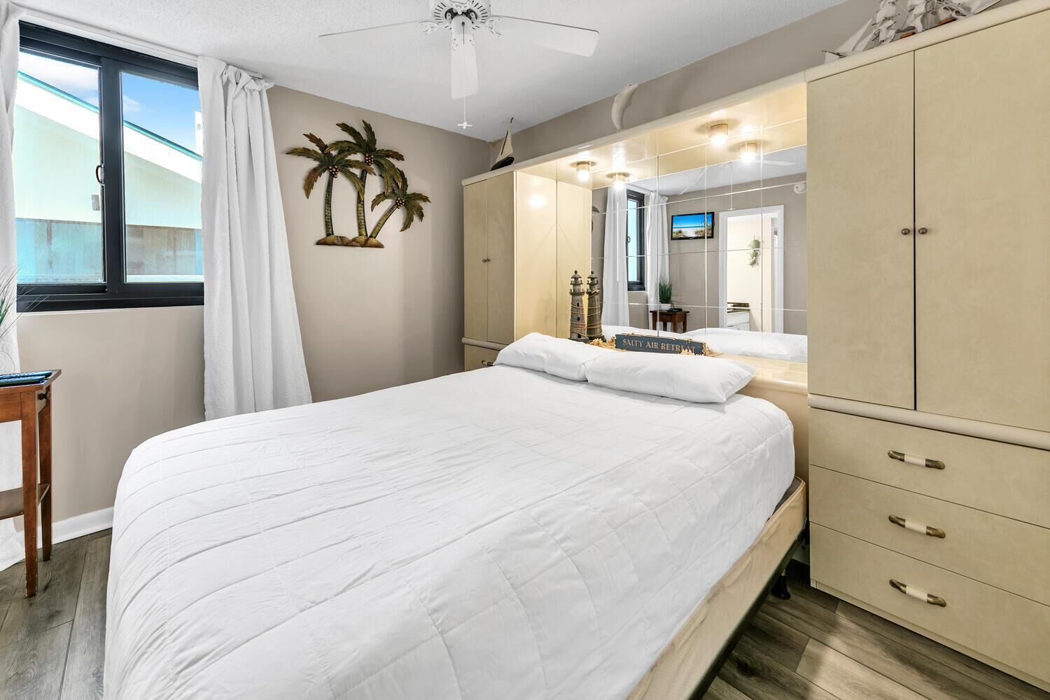 A bedroom with a large bed, a wardrobe, a vanity with a mirror, and a ceiling fan.