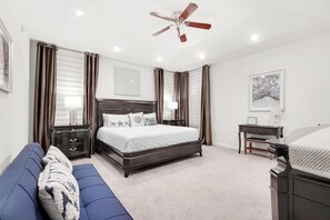 Une chambre à coucher comprenant un lit, un bureau, une chaise, un ventilateur de plafond et une fenêtre avec des rideaux.