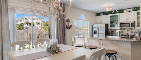 A modern kitchen with white cabinets, a microwave, and a dining area with a chandelier.