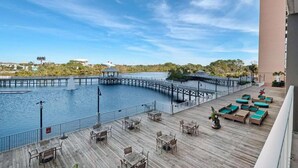 A wooden deck with outdoor seating and a view of a water body with a pier. - Laketown Wharf 116 (Panama City Beach)