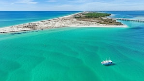 An aerial view of a coastal area with clear turquoise waters, a boat, and a pier extending into the sea. - Palms Resort #2812 Jr. 2br-sunset Dreamer (Destin)
