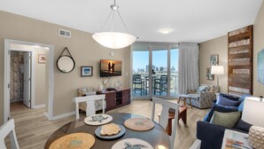 A modern living room with a dining area, large windows, and a city view. - Palms Resort #2812 Jr. 2br-sunset Dreamer (Destin)