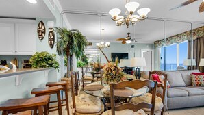 A spacious living area with a round glass table, wooden chairs, a grey sofa, and a ceiling fan. - Majestic Beach Towers 2-1305 (Panama City Beach)