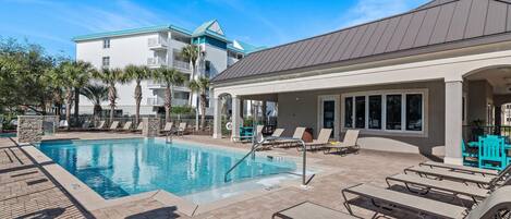 A swimming pool with lounge chairs, a covered area, and a building with balconies.