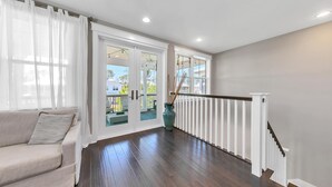 Une pièce spacieuse dotée d’un plancher en bois, d’un canapé beige et donnant, par de grandes portes vitrées, sur un espace extérieur agrémenté d’une terrasse.