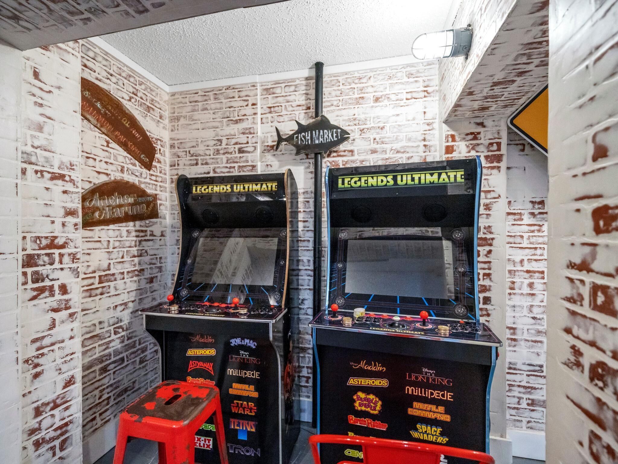 Two arcade machines labeled 'Legends Ultimate' in a room with a brick wall and a 'Fish Market' sign.