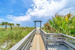 A wooden boardwalk leading to a beach with a pergola structure.