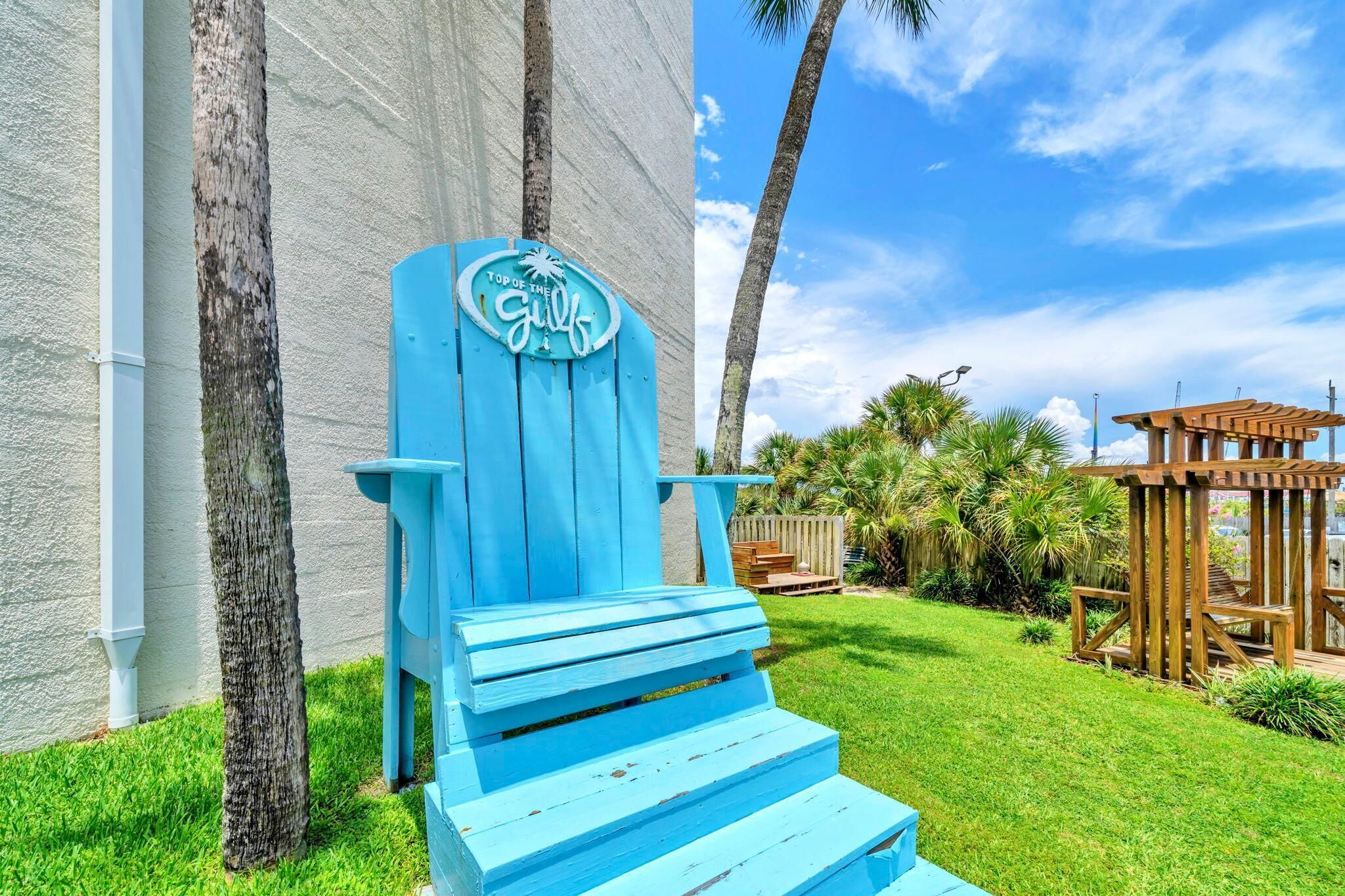 Une chaise Adirondack bleue, ornée d’une pancarte indiquant « Meilleur établissement de la ville », un mur blanc et une pergola en bois, le tout dans un cadre extérieur ensoleillé.