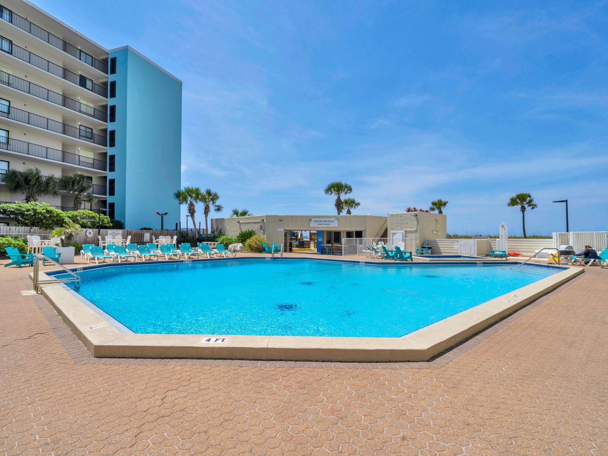 A swimming pool with lounge chairs, a building with balconies, and palm trees.