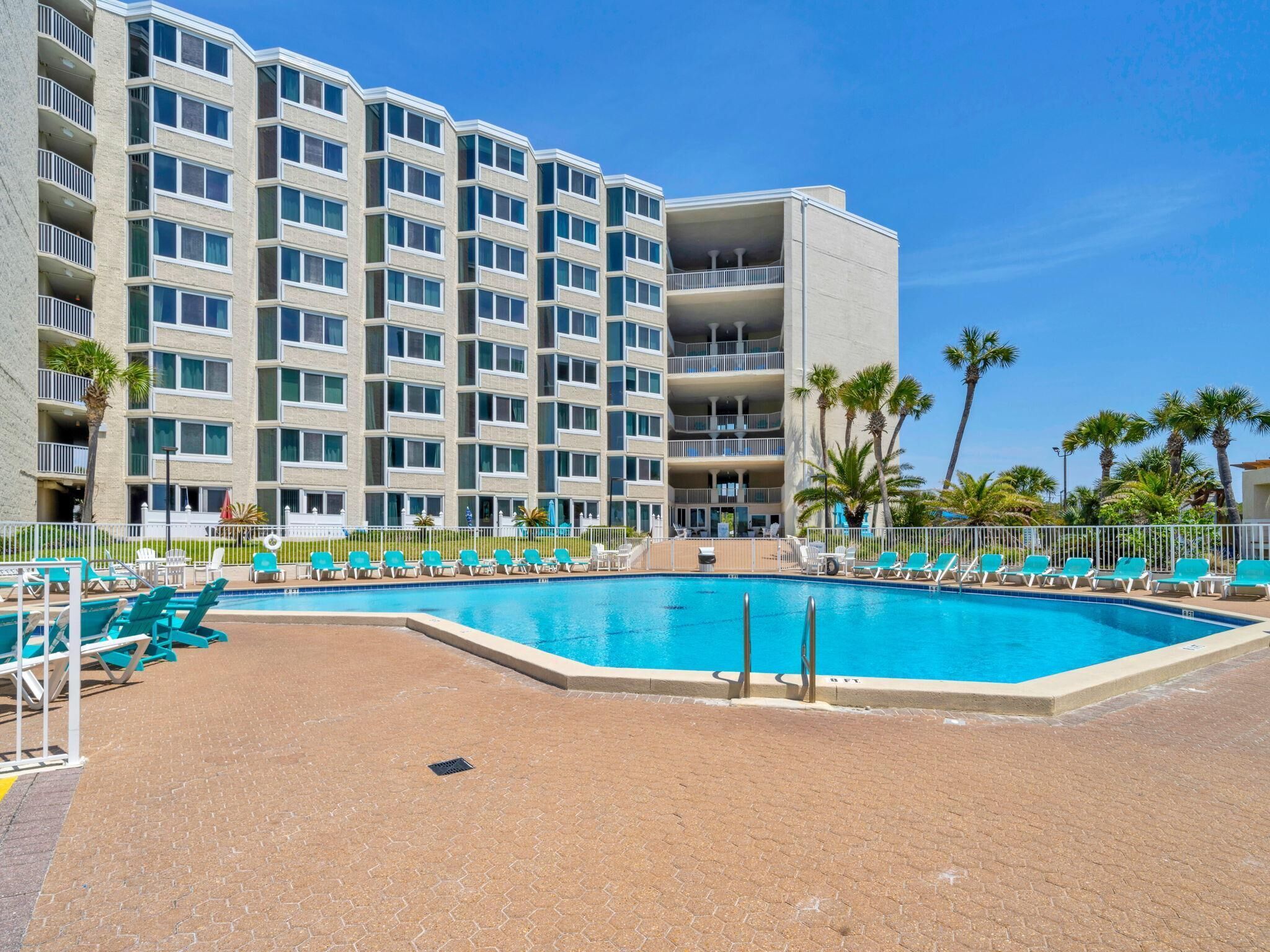 A hotel with a swimming pool, multiple balconies, and palm trees.
